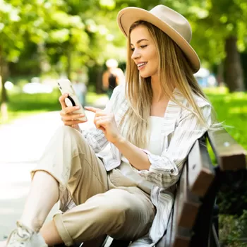 young woman using phone in park sitting on bench